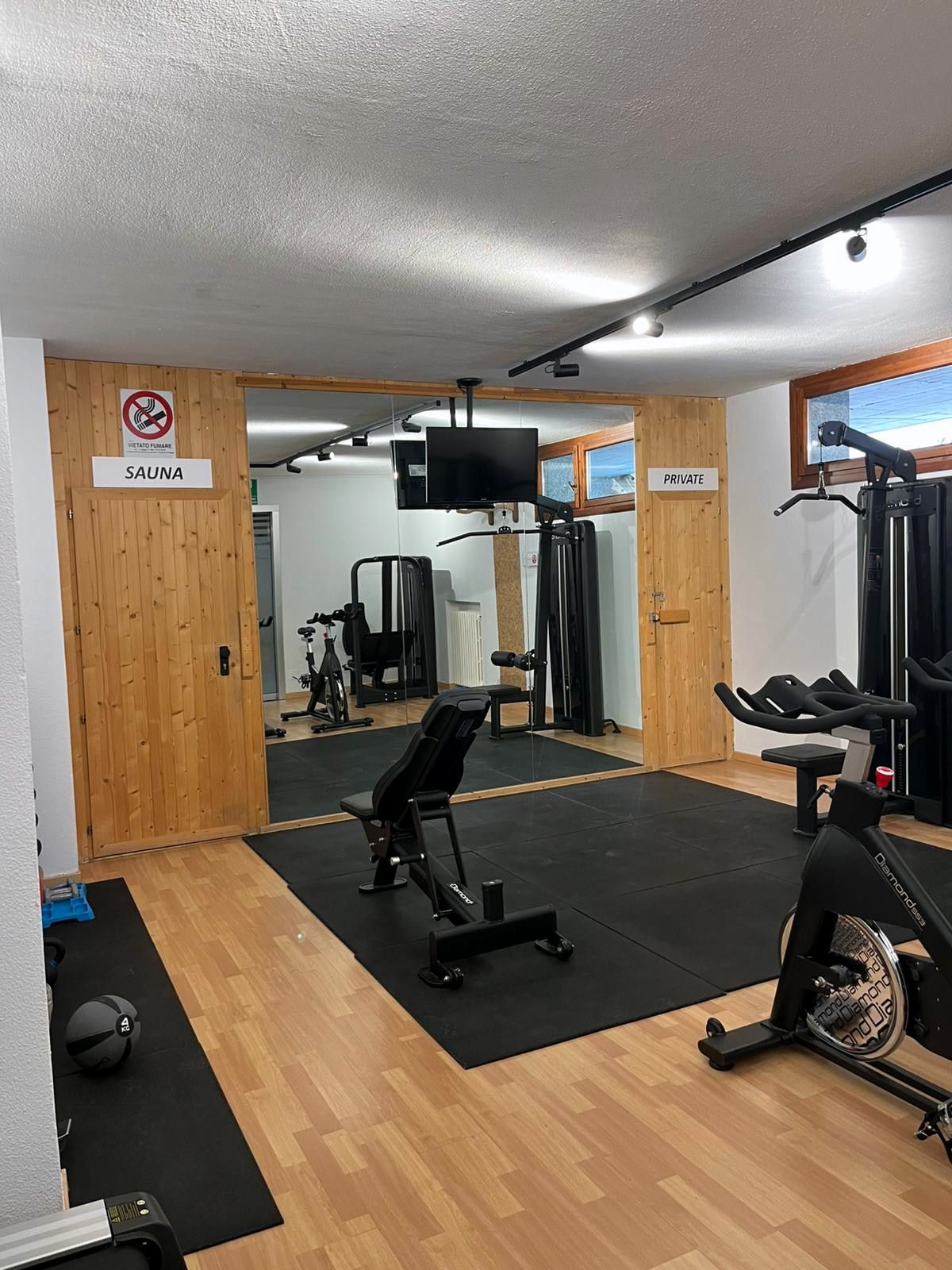 Palestra del residence con panca, attrezzi e porta in legno della sauna